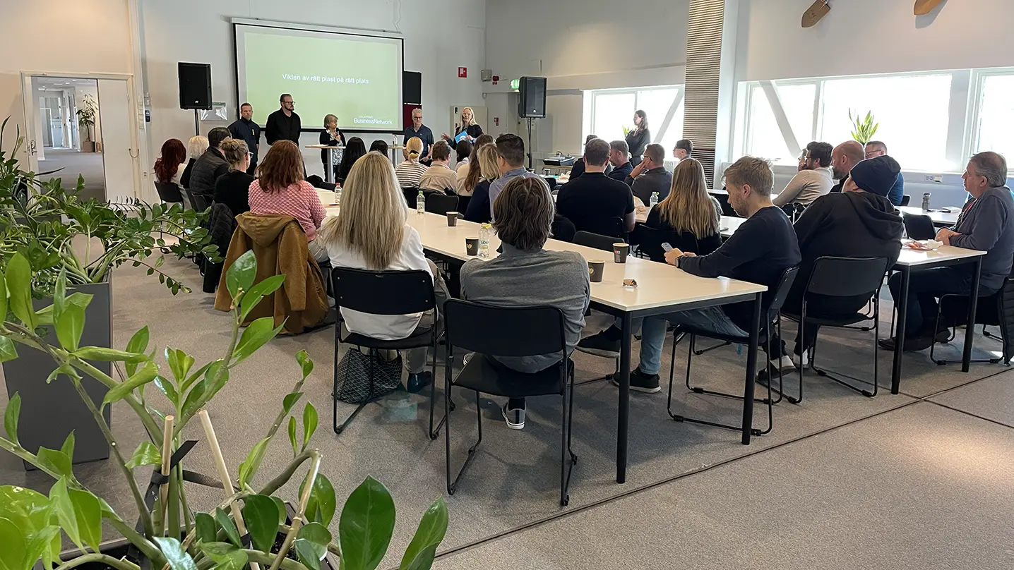 Människor sitter runt bord och tittar på fyra personer som håller en presentation.