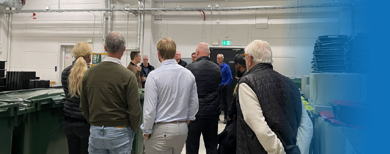 En grupp människor står mellan avfallspåsar och avfallskärl.