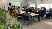 Människor sitter runt bord och tittar på fyra personer som håller en presentation.